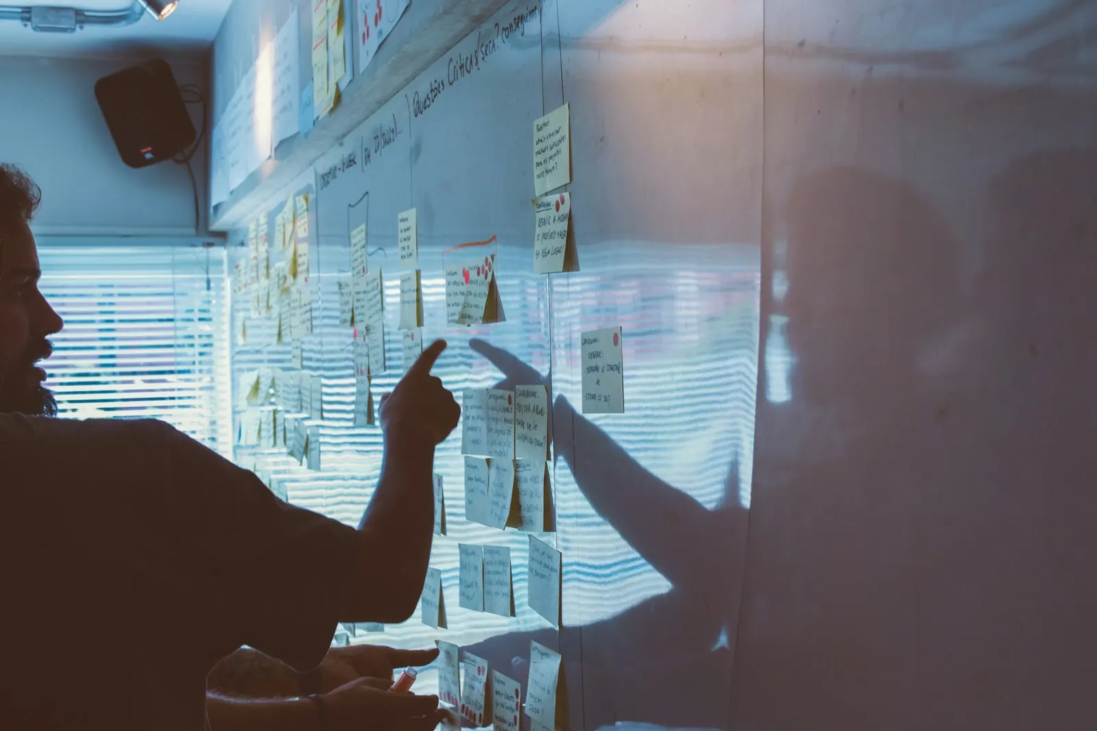 Duas pessoas apontando para um mural de post-its iluminado